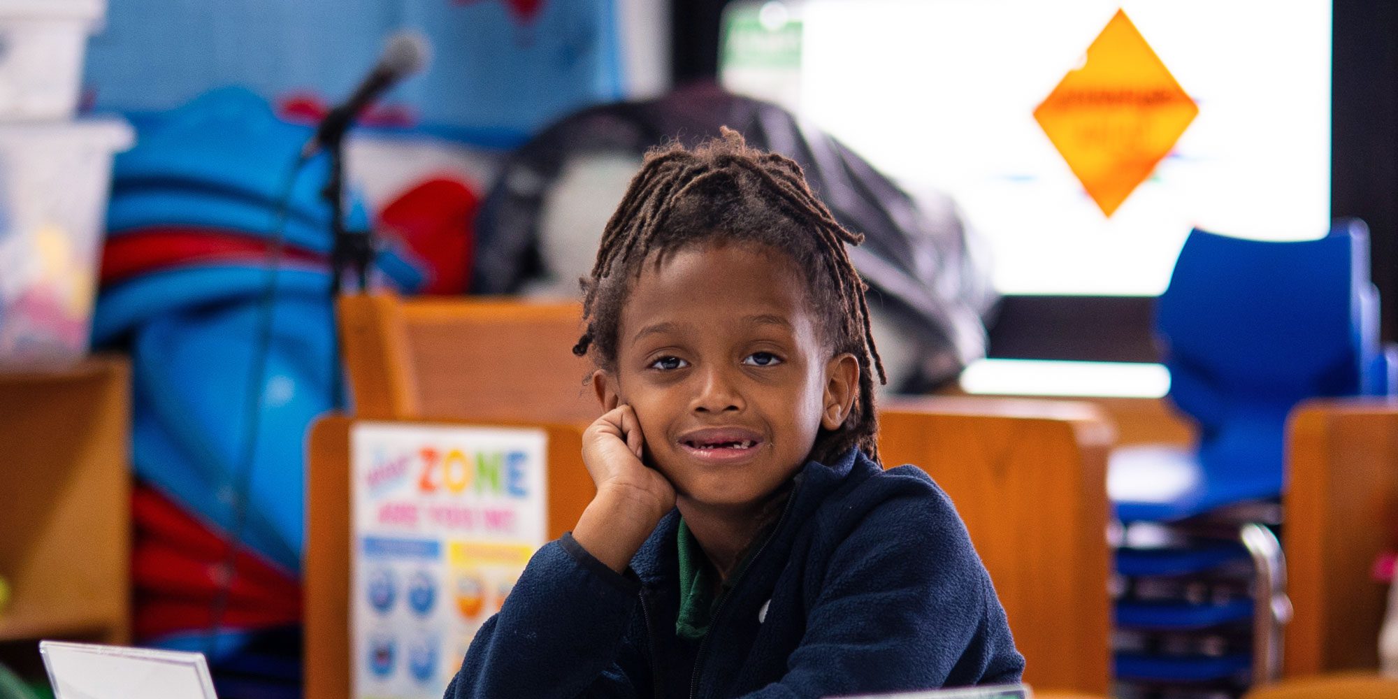 Smiling student with locs resting their cheek on their hand in a classroom.