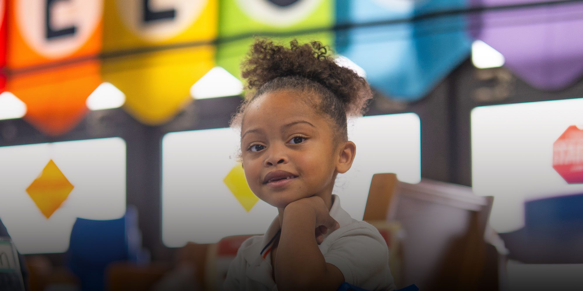 Young student resting their chin on their hand in a colorful classroom.