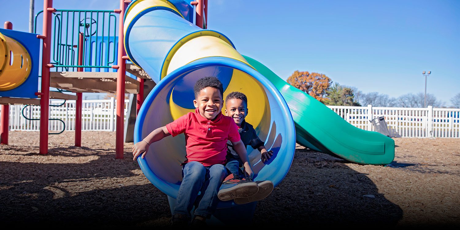 Smiling students sitting on playground slide.